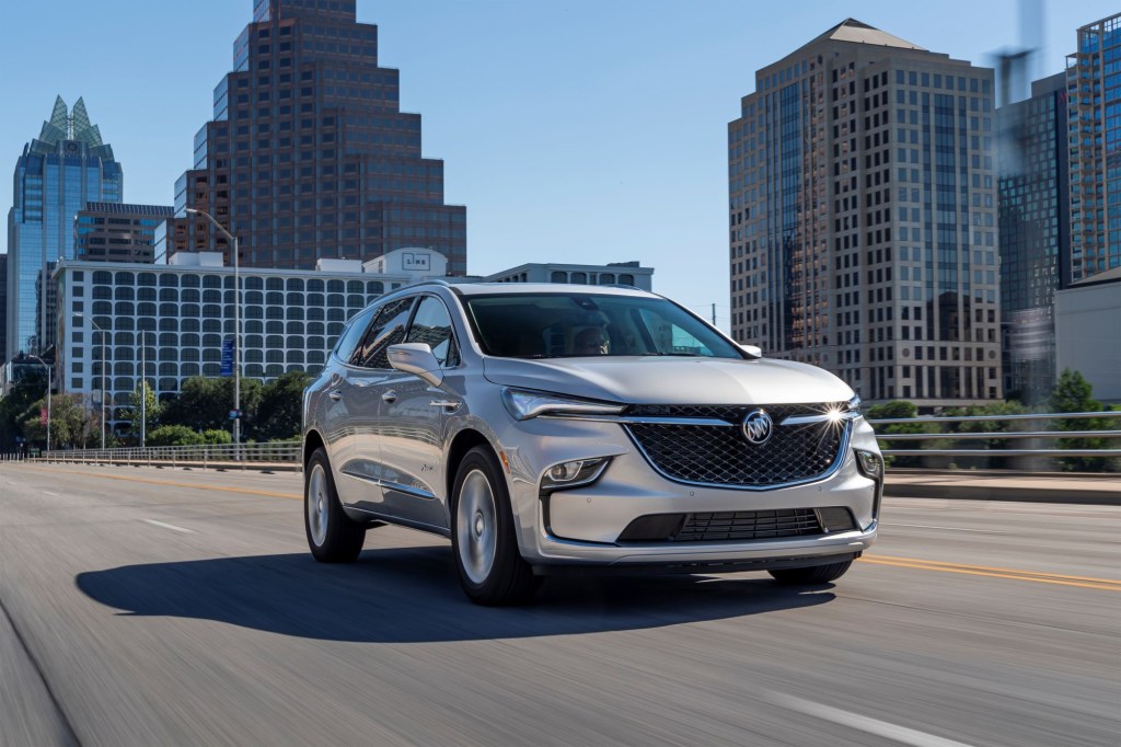 A silver 2022 Buick Enclave driving through a city surrounded by sky scrapers driving on a highway.