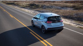 A silver 2022 Chevy Bolt EV travels on a two-lane highway along a large body of water on a sunny day