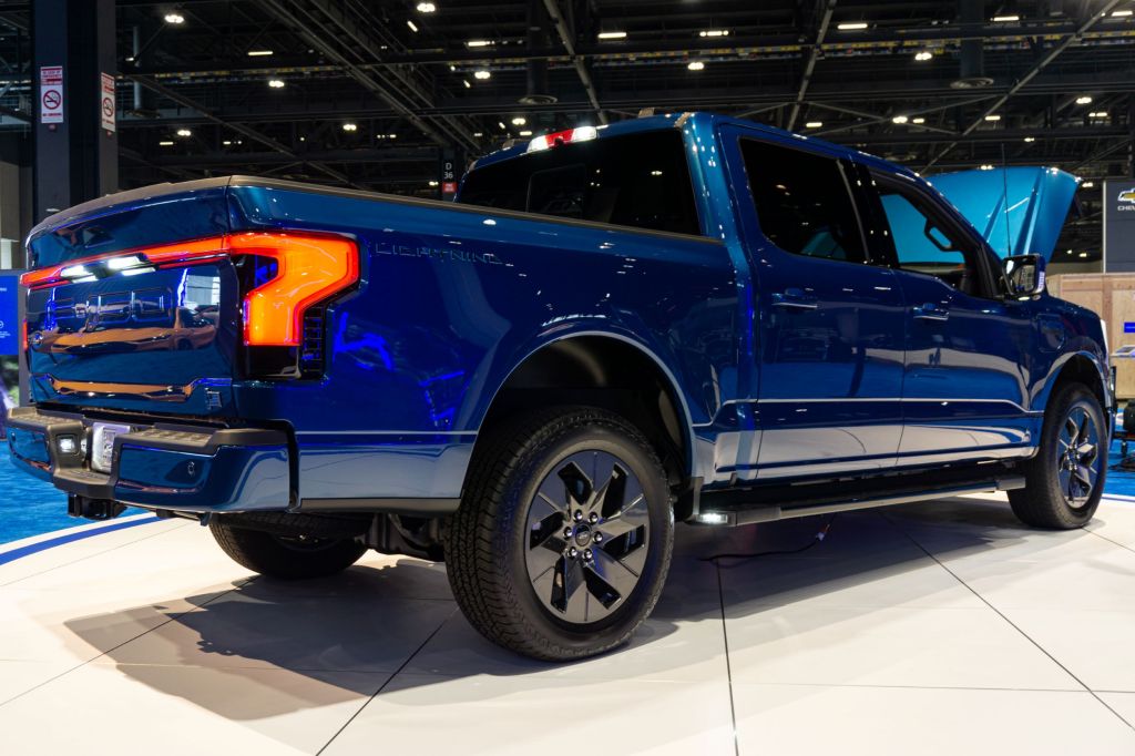 The rear 3/4 view of a blue 2022 Ford F-150 Lightning with its frunk open at the 2021 Chicago Auto Show