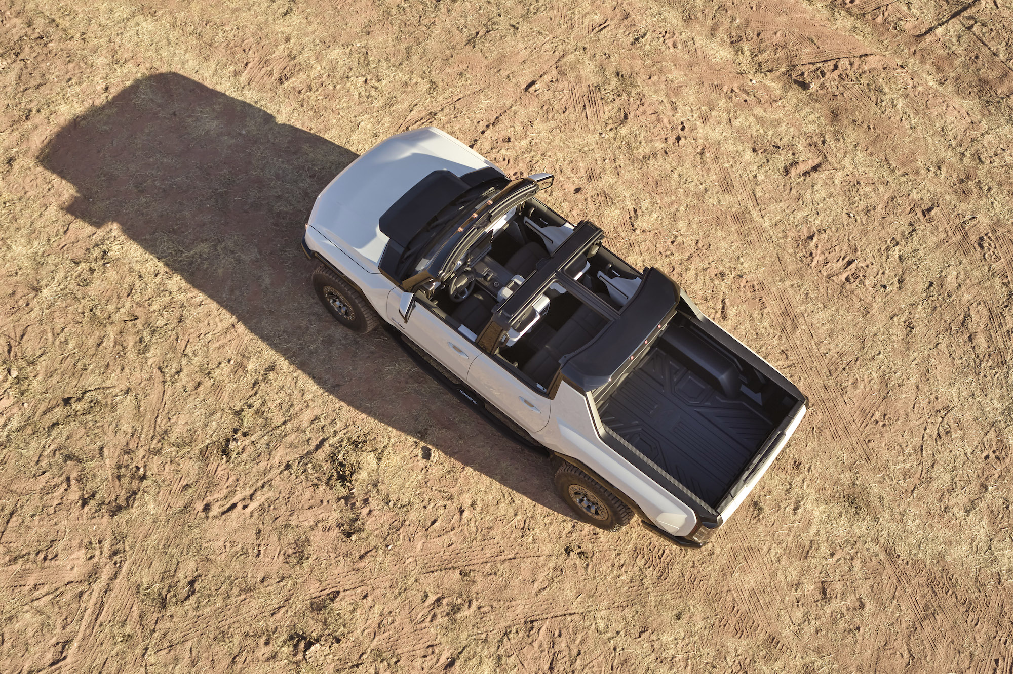 An overhead view of the 2022 GMC Hummer EV, parked on an expanse of beige dirt, with its roof removed