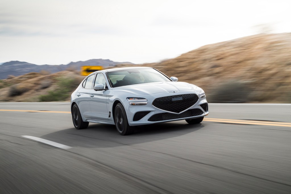 A white 2022 Genesis G70 rounding a curve on an empty road, the G70 is one of the best affordable AWD sedans of 2021