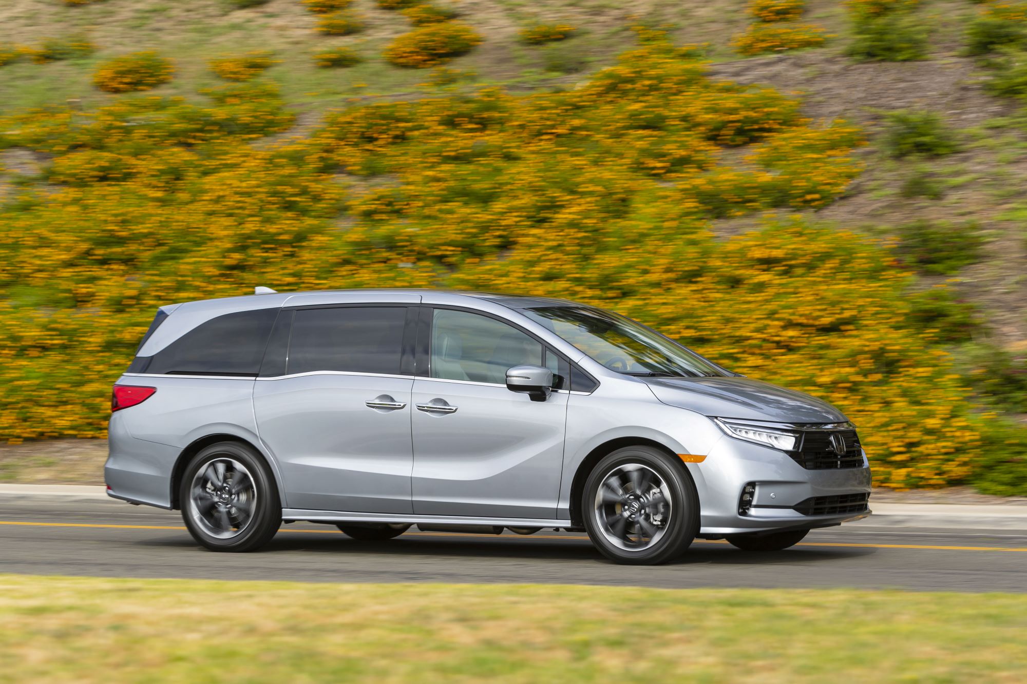 A gray 2022 Honda Odyssey minivan driving on a highway near a grassy hill