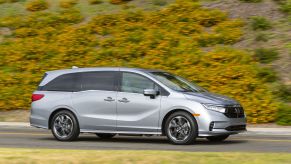 A gray 2022 Honda Odyssey minivan driving on a highway near a grassy hill