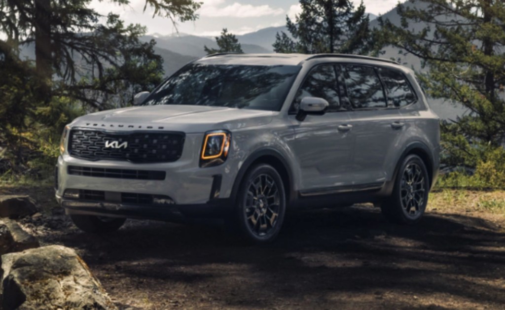 a white 2022 Kia Telluride in a forest with mountains in the background