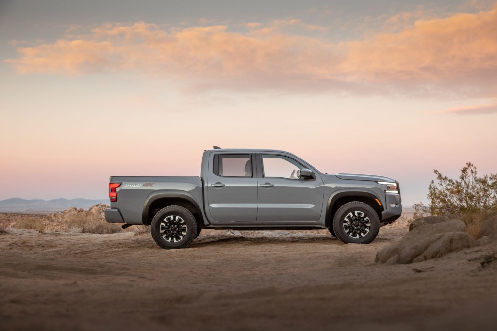 A Silver Nissan Frontier in a desert area with a slightly cloudy sunset colored sky in the background.