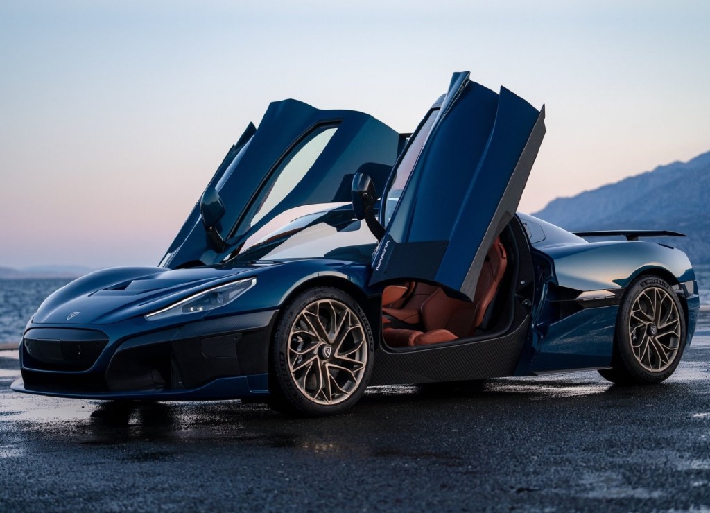 A dark-blue 2022 Rimac Nevera electric supercar with its doors up parked by the ocean