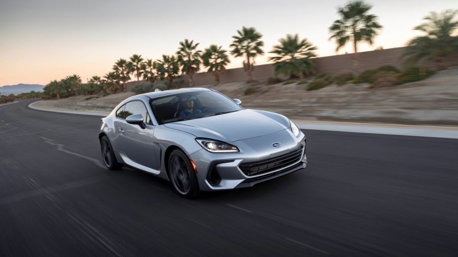 A silver 2022 Subaru BRZ driving down a road in a desert tropical area with sand and palm trees.