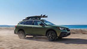 A green 2021 Subaru Outback with surfboards on top.