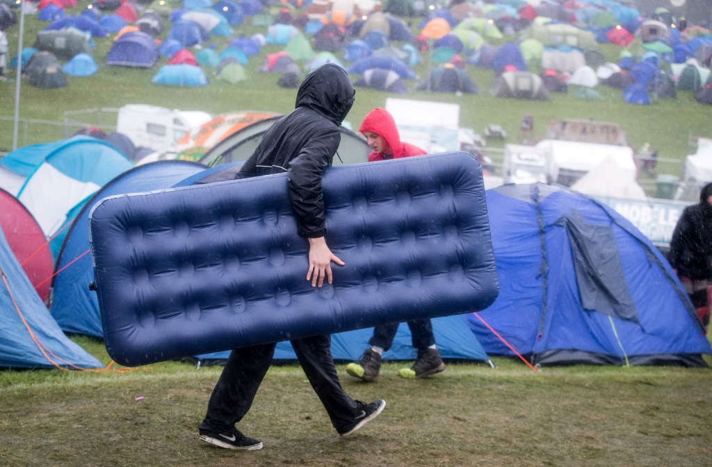 A man carrying an air mattress into a festival as it rains