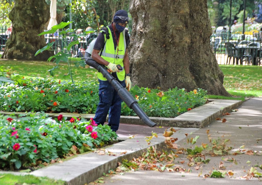 A city work in a yellow vest operating a leaf blower