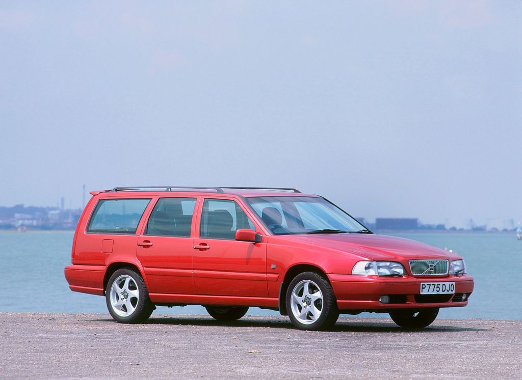 A red Volvo station wagon parked on a beach near the sea