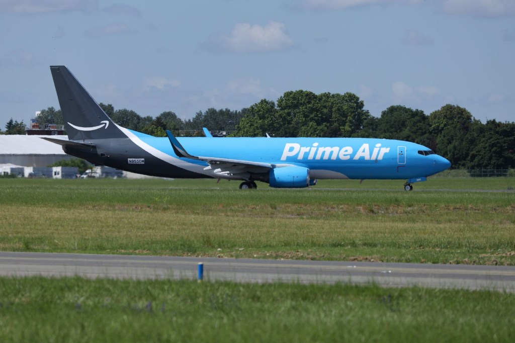 A blue, black, and white Amazon Prime Air Boeing 737 aircraft parked in an air field