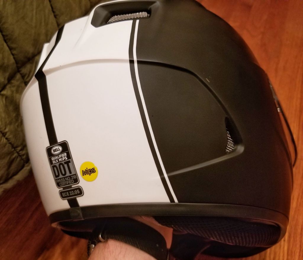 The rear view of a black-and-white Bell Qualifier DLX MIPS motorcycle helmet showing the DOT, ECE, and MIPS stickers