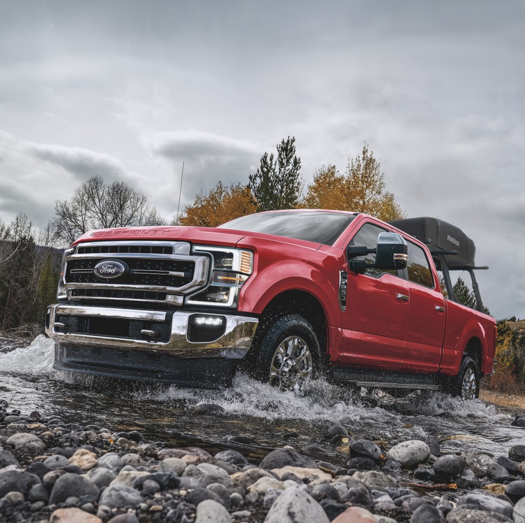 A red Ford F-Series truck plows its way through a rocky stream