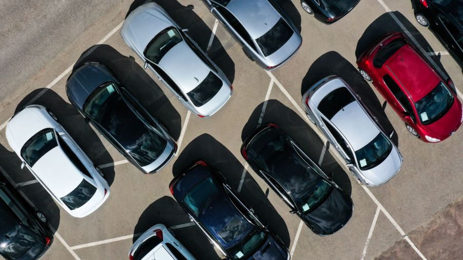 A group of cars in a dealership parking lot ranging in colors from black, red, and silver.