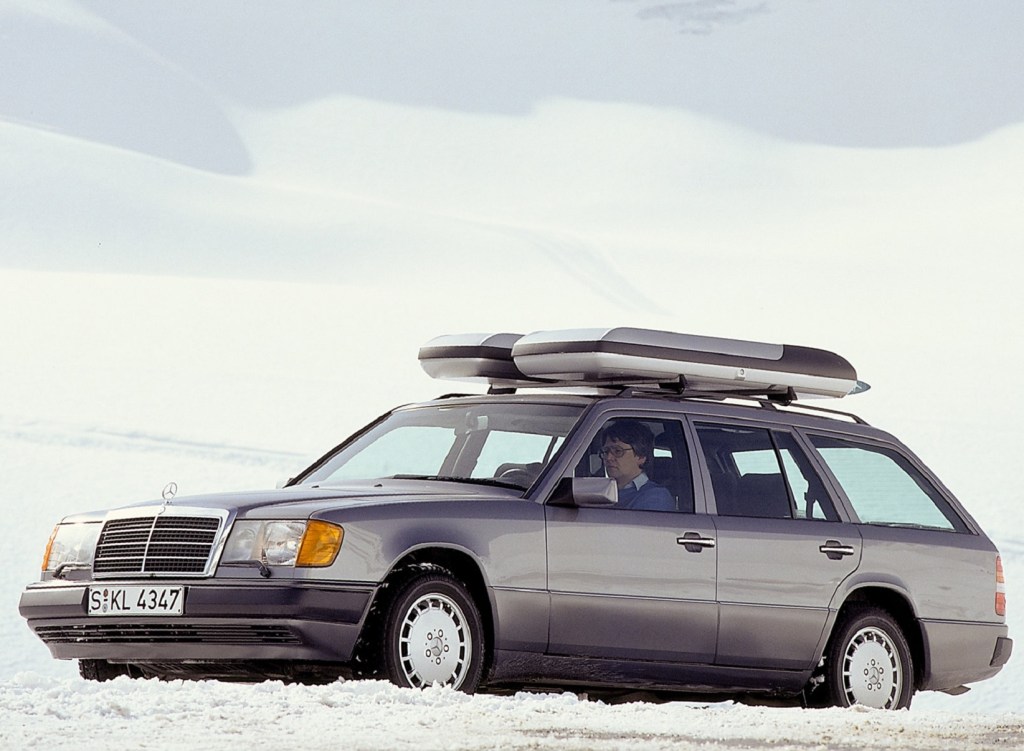 A silver 1988 Mercedes E-Class Estate with roof boxes on a snow-covered mountain