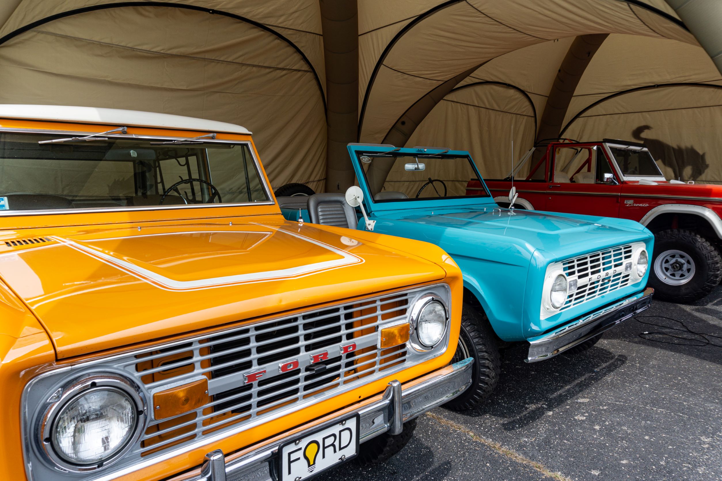 An orange, turquoise, and a red-and-white classic Ford Bronco under a tent outside the 2021 Chicago Auto Show