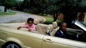 A father driving a gold convertible with his daughter in the back seat