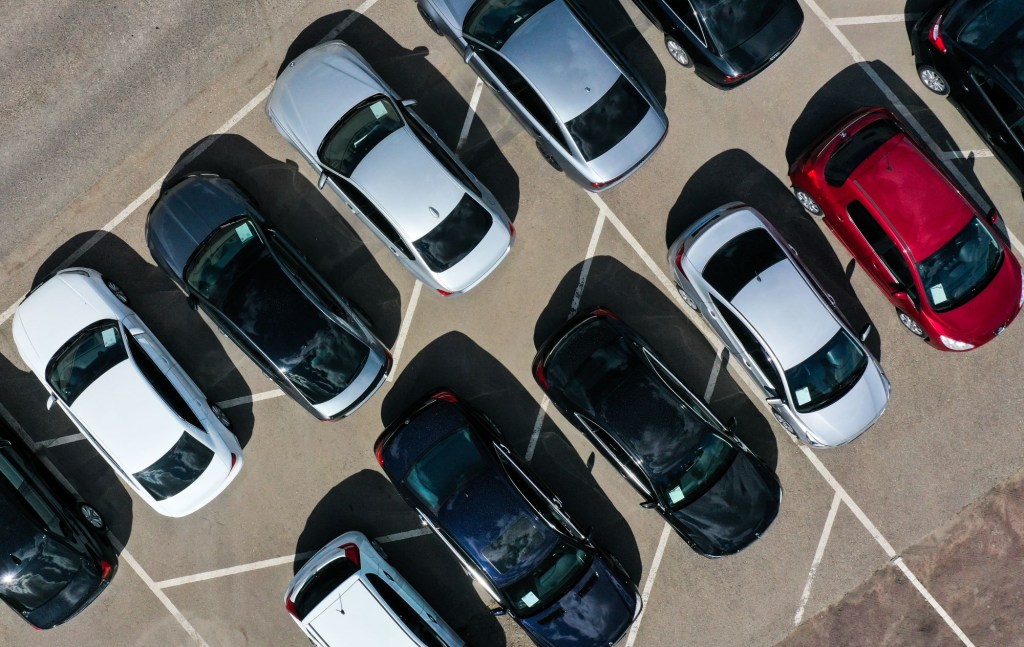 A car parking lot with two rows of 6 cars of mixed colors with black, silver, and red cars.