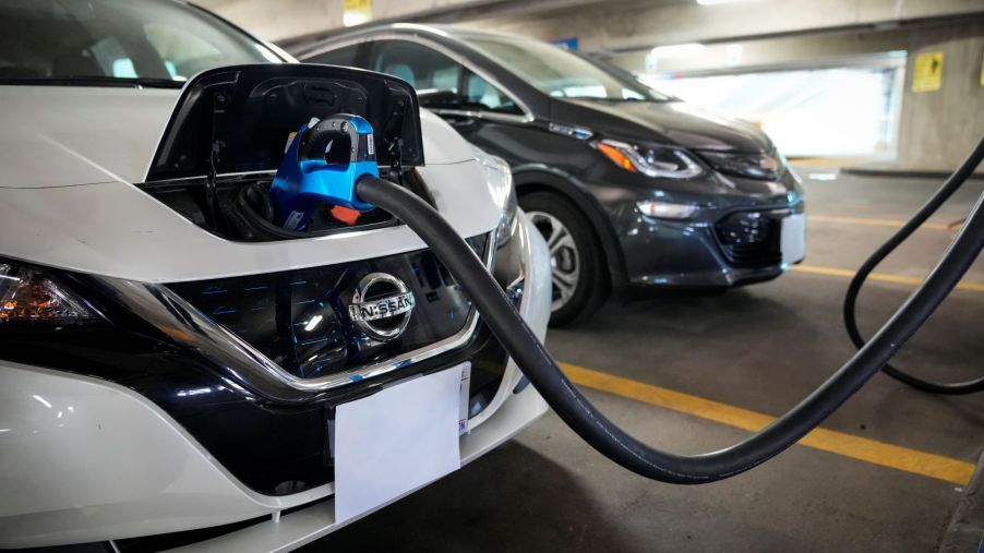 A Nissan Leaf EV plugged into an electric charging station in a parking garage