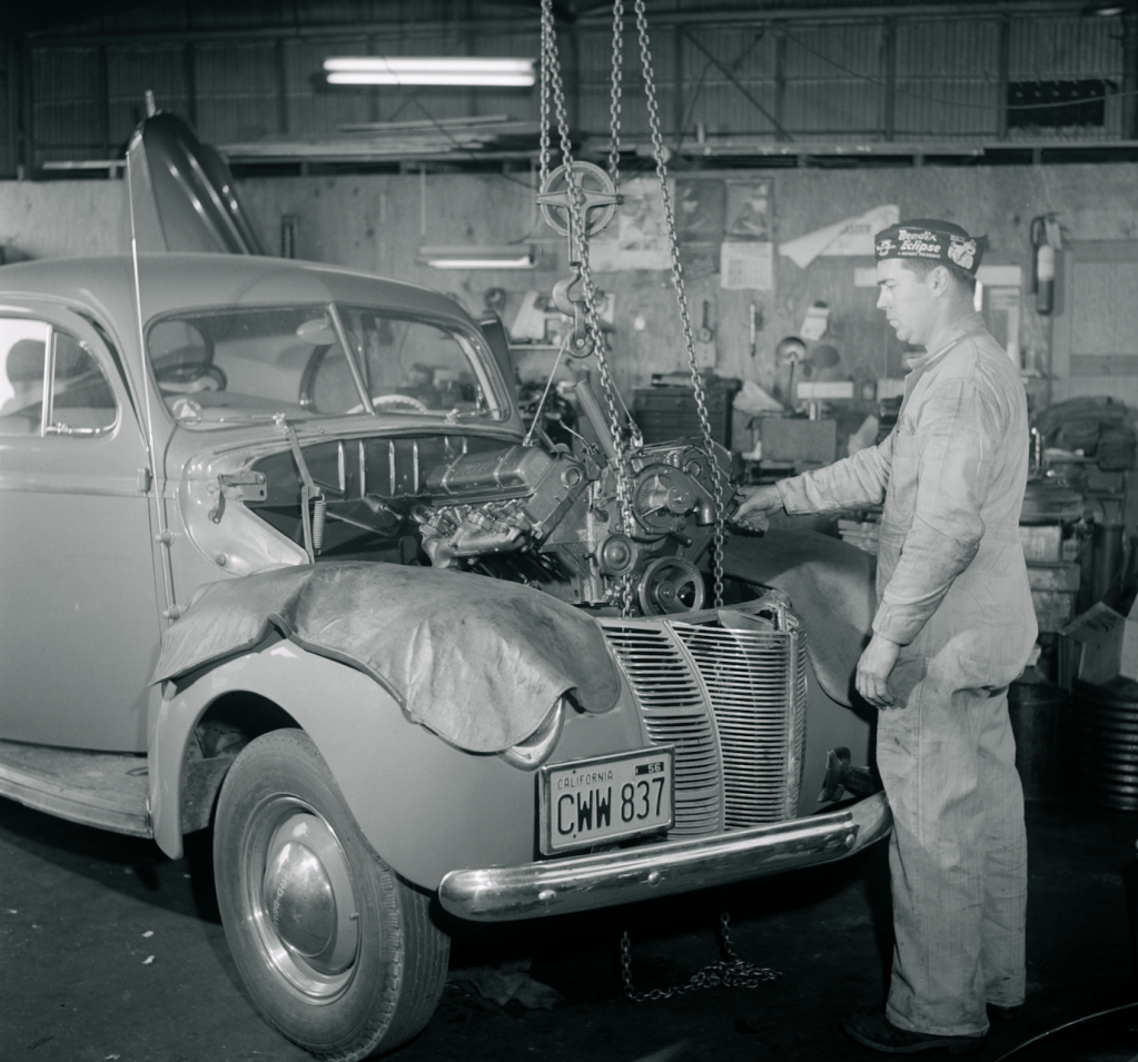 mechanic pulling engine out of a 1940 Ford