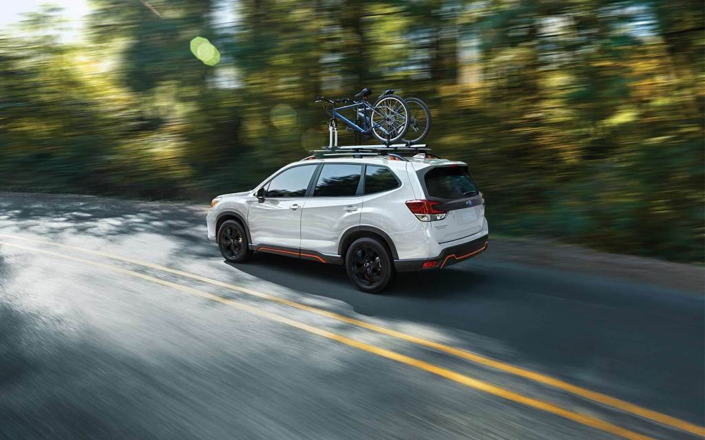 A white 2021 Subaru Forester driving with a bicycle on top.