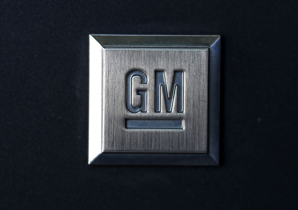 A charcoal grey plaque with the General Motors logo, GM, on it against a black background. 