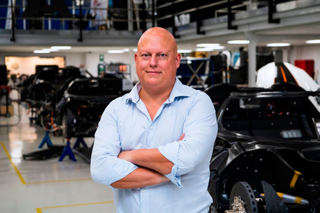 Christian von Koenigsegg stands with arms folded at his factory. with partially assembled cars in the background