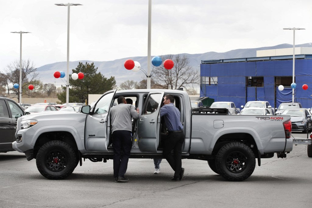 A group of men crowd around a new Tacoma on a dealership lot