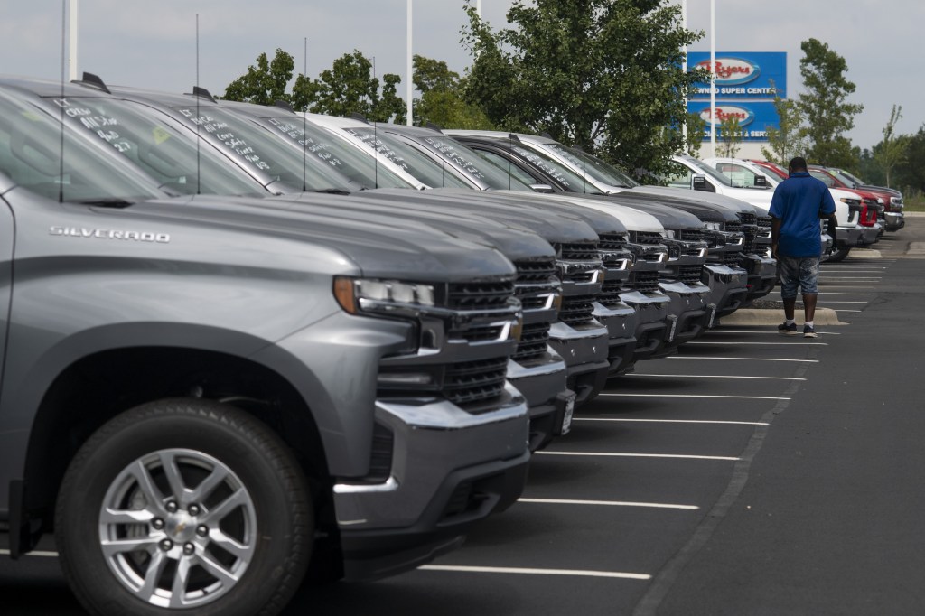 A man examines a row of Chevy pickup trucks at a dealership