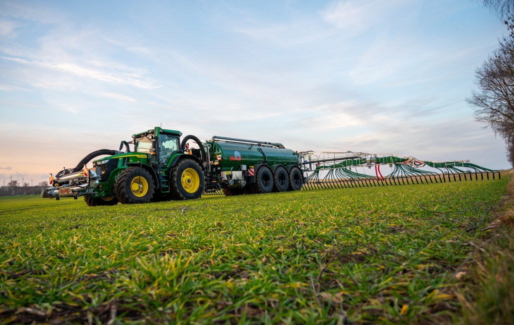 A farmer spreads liquid manure on a field with his team in a giant John Deere tractor farming machine 