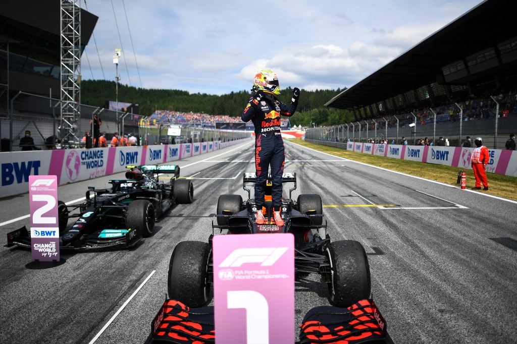 Max Verstappen stands, hands raised, on the top of his F1 car after winning the Austrian Grand Prix