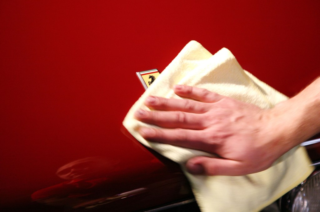 A man runs a microfiber cloth over the hood of a red Ferrari 250 GT