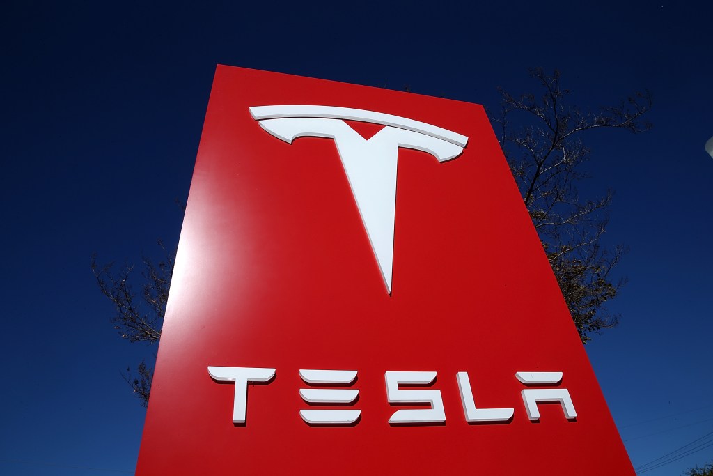 A red sign featuring white font that reads "Tesla" with the brand's logo across the top