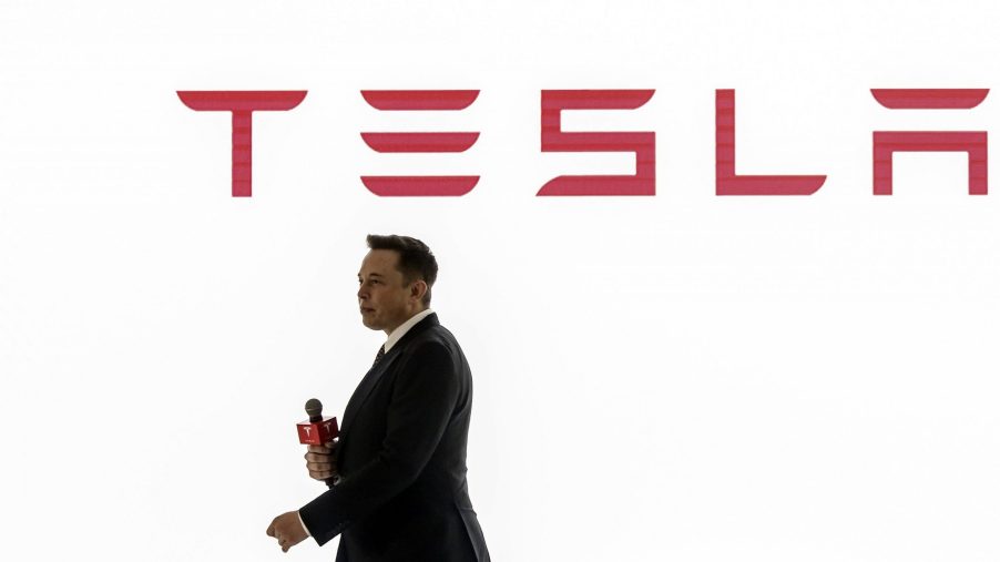 Tesla CEO Elon Musk presents at a conference with the brand's logo seen in red on a white background behind him