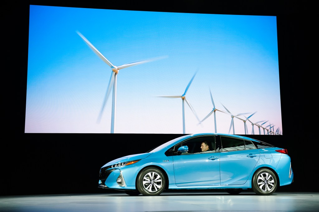 A bright blue hybrid Prius Prime posing in front of a windmill graphic