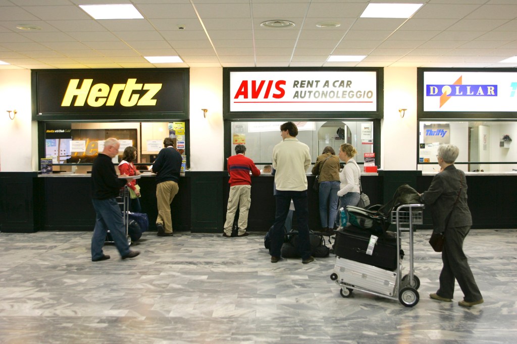 A rental car desk, shown with agents filling out paperwork and selling rental car insurance
