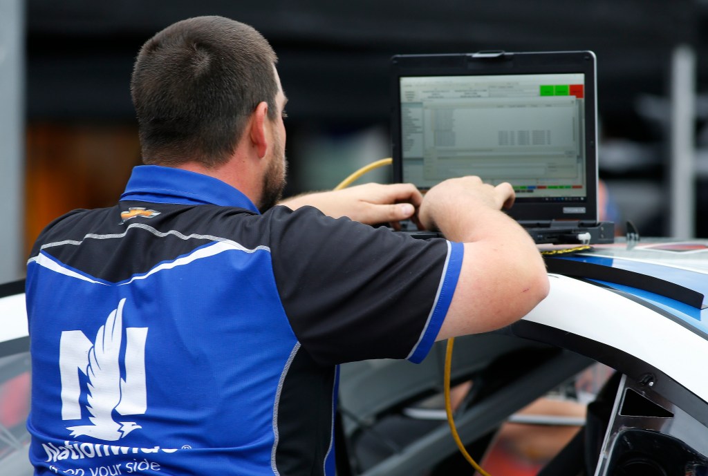 A NASCAR pit mechanic works on a laptop