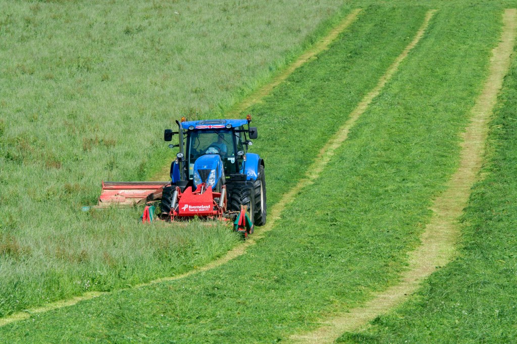 a new holland tractor cutting a hay field 