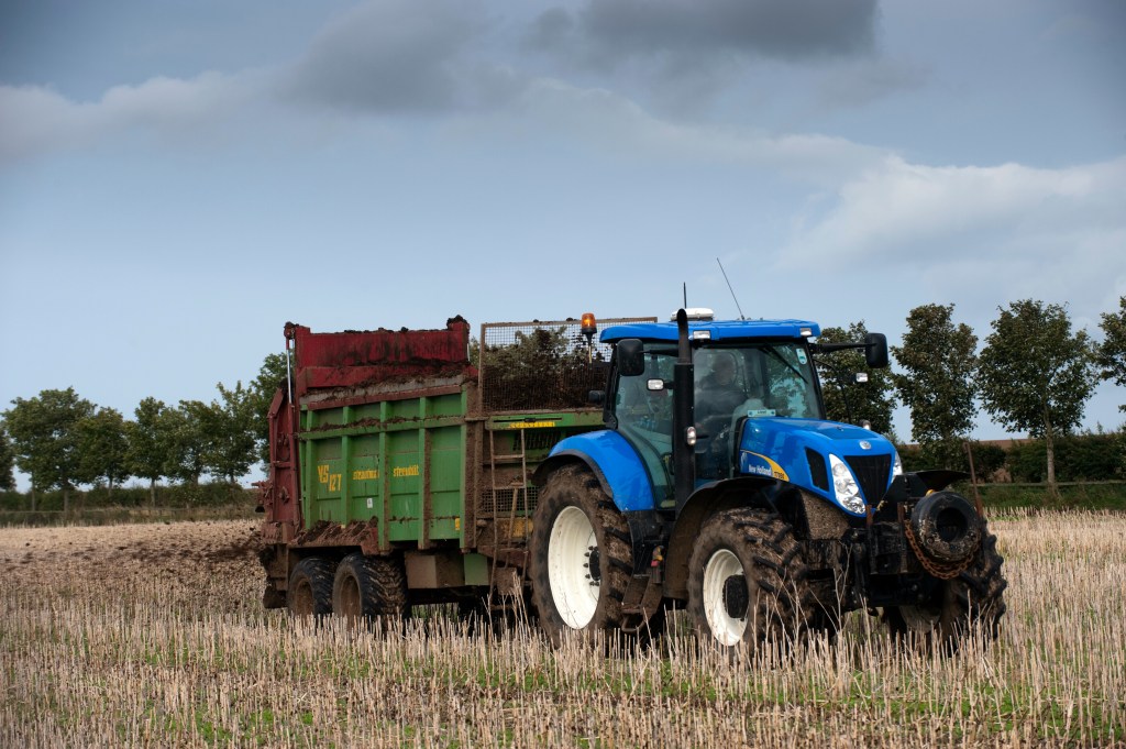 a new holland tractor spreading manure in an agricultural field 