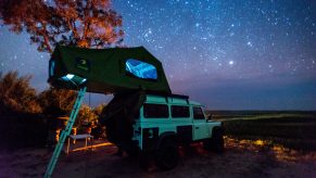 A Land Rover with a roof tent parked under the stars