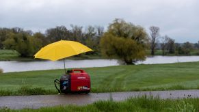 A Honda generator under a yellow umbrella on a trail next to a river