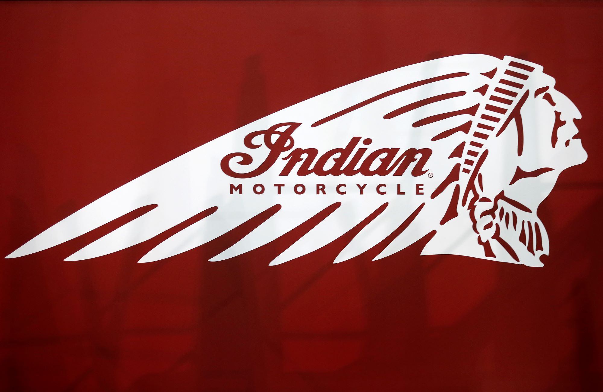 A white Indian Motorcycle logo on a red background with some vague shadows behind it.