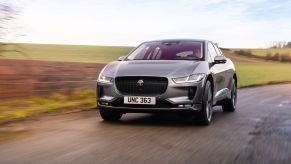 A silver Jaguar I-Pace driving on a highway with a background of green plains.
