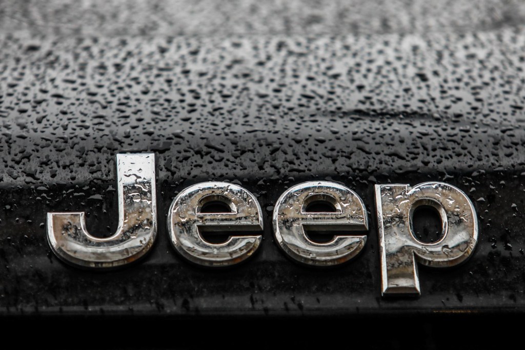 Jeep's logo in silver on a black car with raindrops.