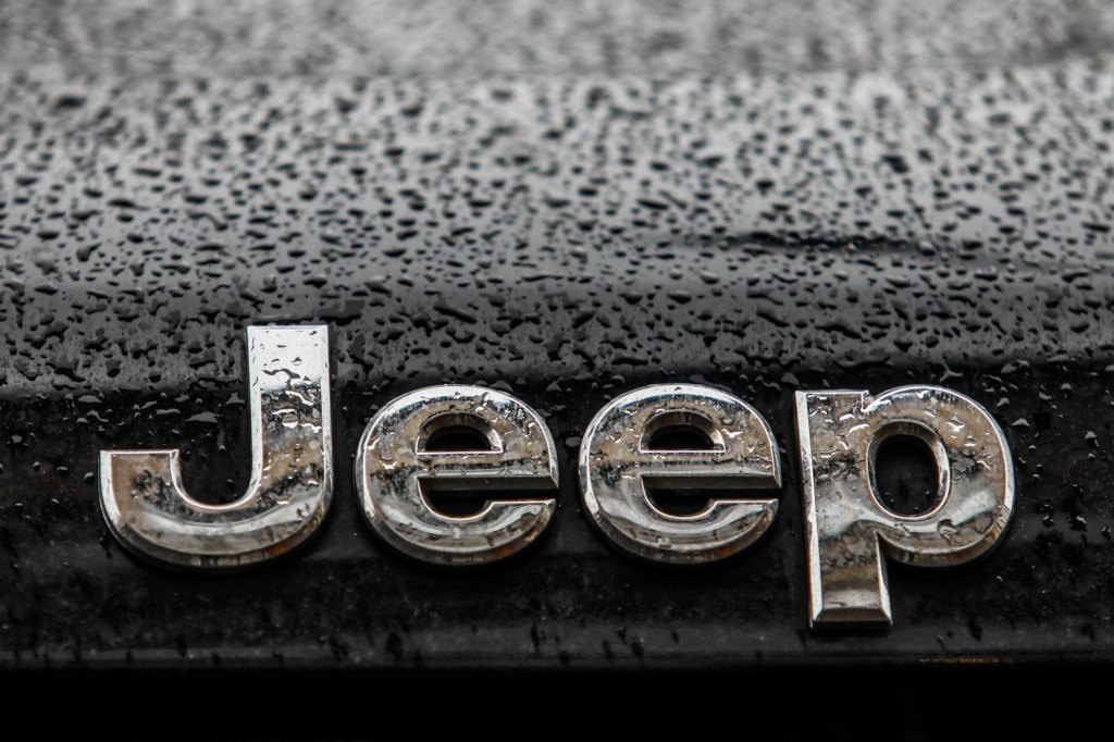Jeep's logo in silver on a black car with raindrops. 