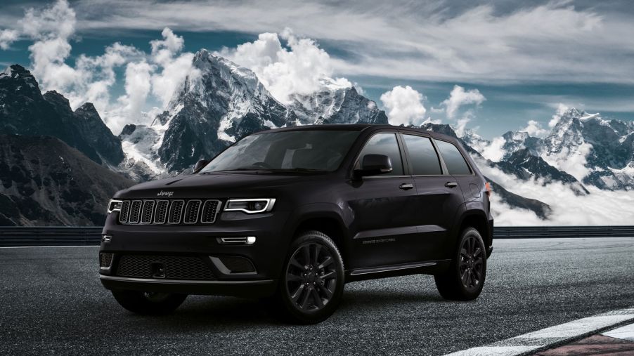A black Jeep Grand Cherokee model parked on a racetrack near snowy and cloudy mountains