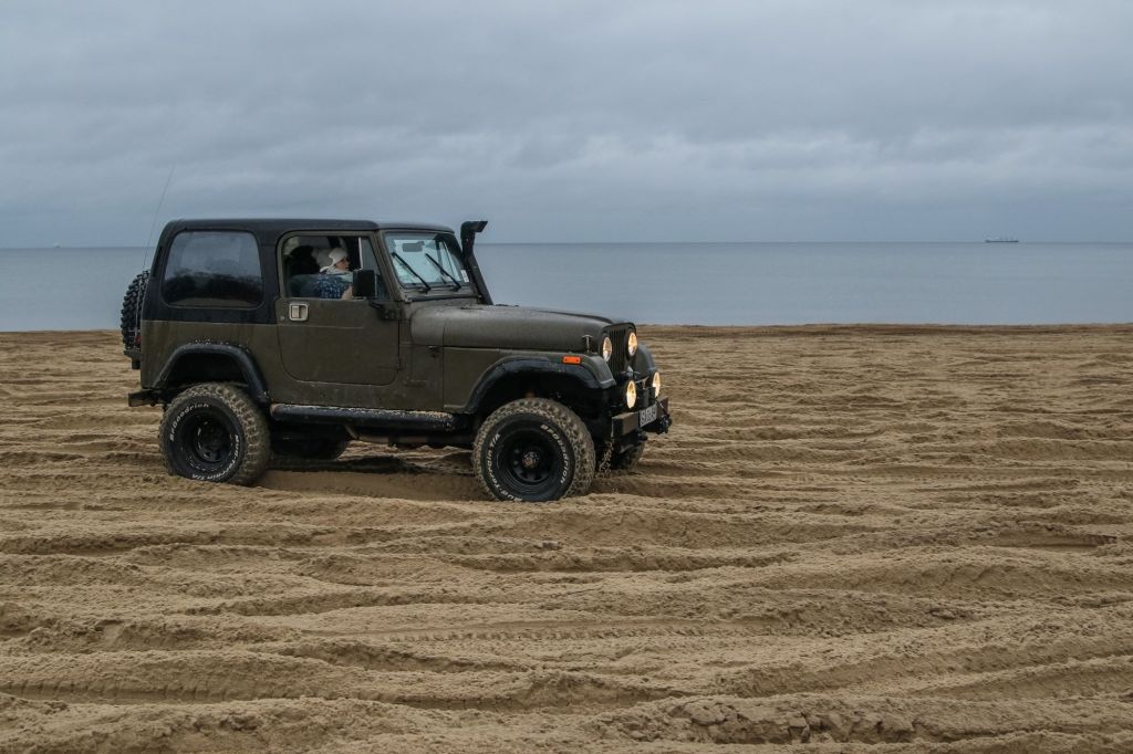 A Jeep Wrangler military model driving on a Baltic Sea coast beach