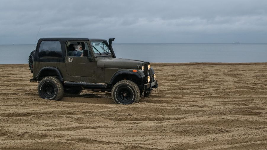 A Jeep Wrangler military model driving on a Baltic Sea coast beach