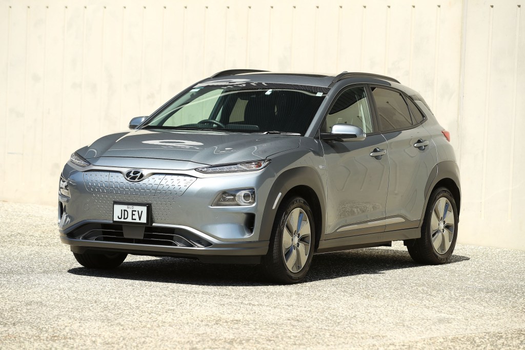 A silver Hyundai Kona Electric SUV parked in gravel outside a concrete building